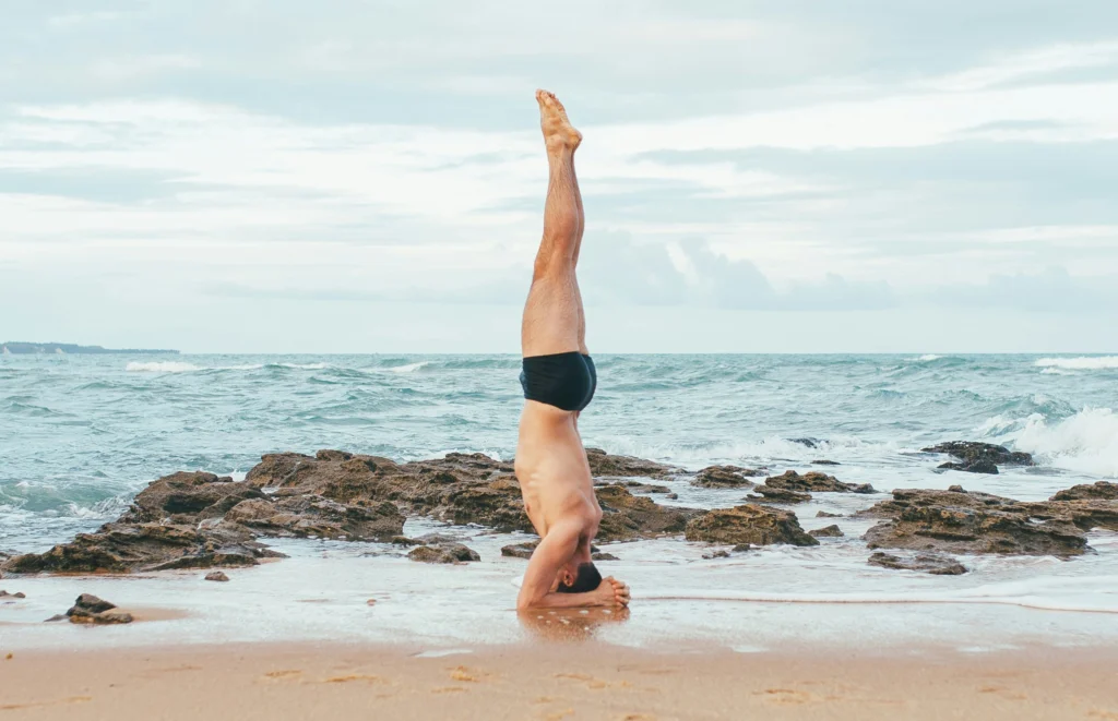 Mężczyzna wykonuje sirasanę (stanie na głowie) na plaży